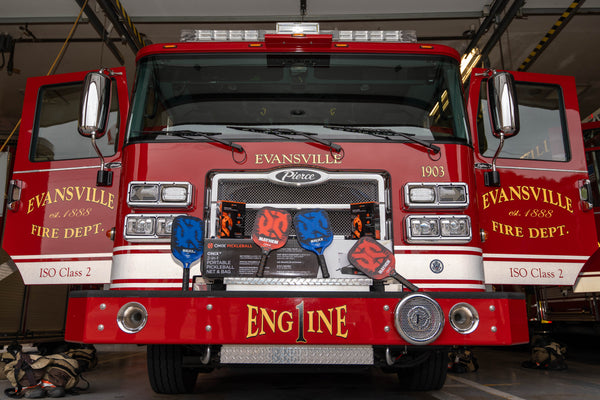 Evansville Fire Department truck with pickleball paddles, balls, and a net sitting on the front bumper